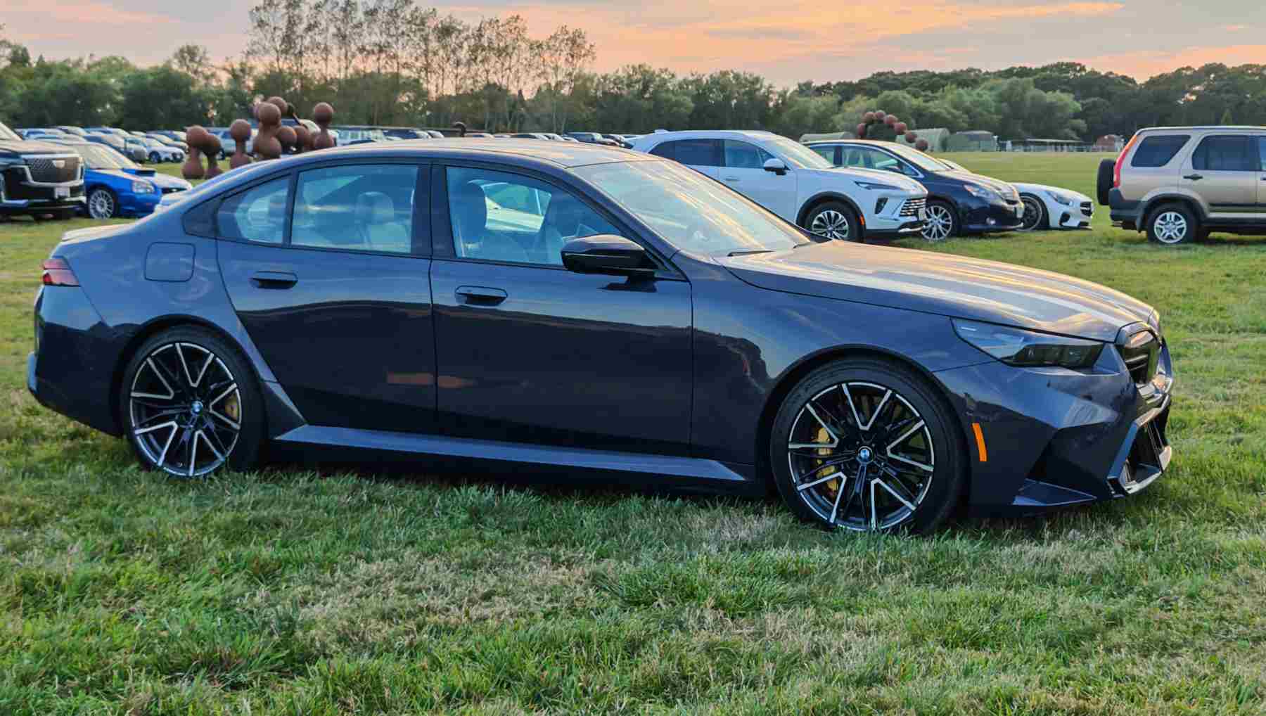 A blue 2025 BMW M5 parked in a field at sunset