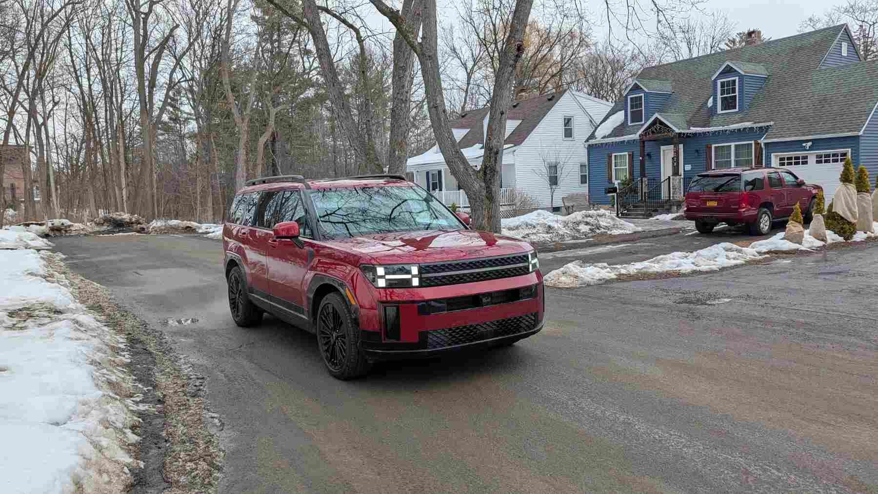 Front 3/4 view of a red 2026 Hyundai Santa Fe in the suburbs