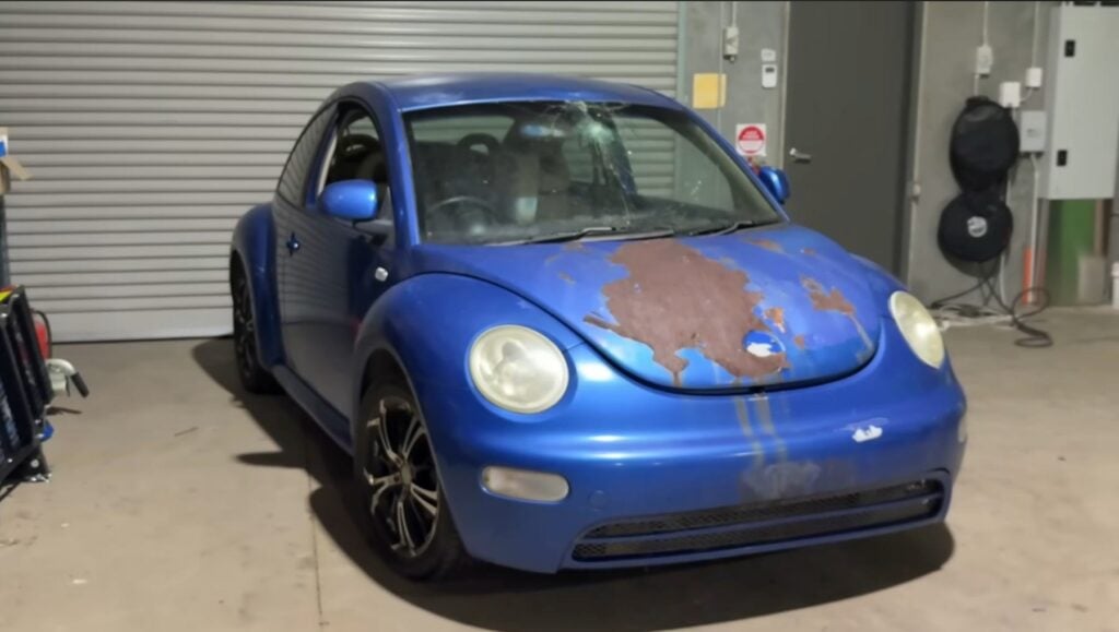 A rusted, damaged, blue VW new beetle
