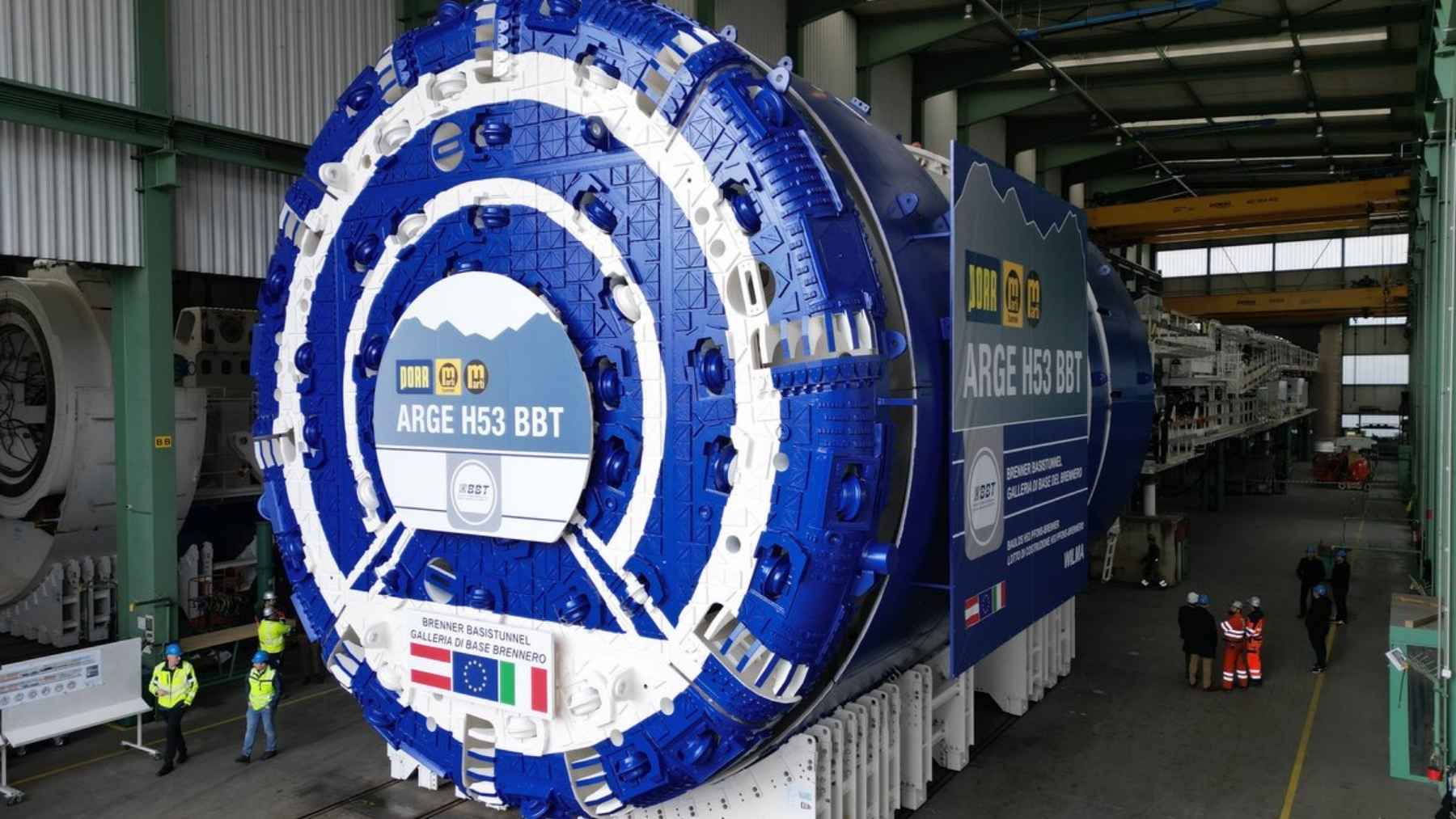 A 6-million-pound machine named Wilma was shipped to Austria in 80,000 pieces across 170 special loads, rebuilt in a chamber cut into the mountain, and spent 706 days boring north until she broke into a 34-mile hole that crews had dug toward her from another country