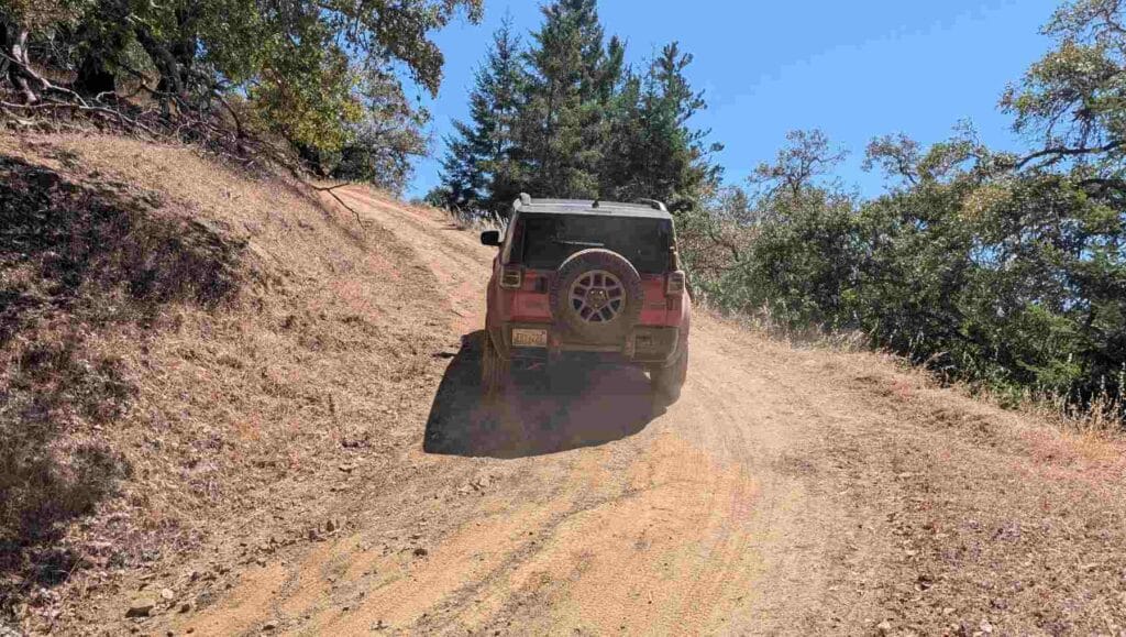A rear view of a red 2026 Jeep Recon ascending a steep track