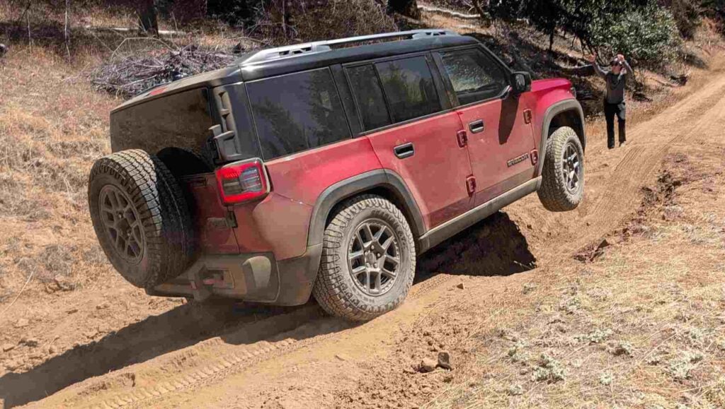 A view of a red 2026 Jeep Recon on rough terrain with a wheel in the air