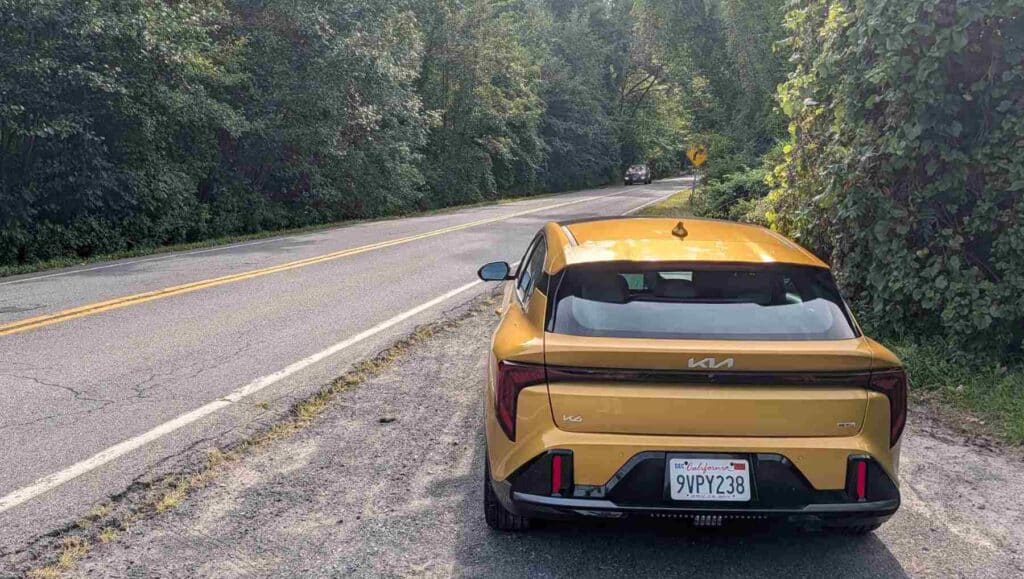 A rear view of a gold 2026 Kia K4 pulling out onto a road