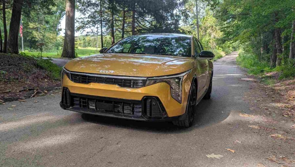 A front view of a gold 2026 Kia K4 on a wooded trail