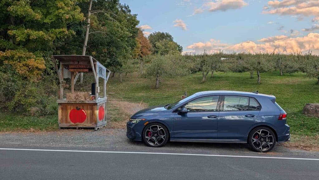 A A side view of a blue 2026 Volkswagen Golf GTI parked near an apple stall